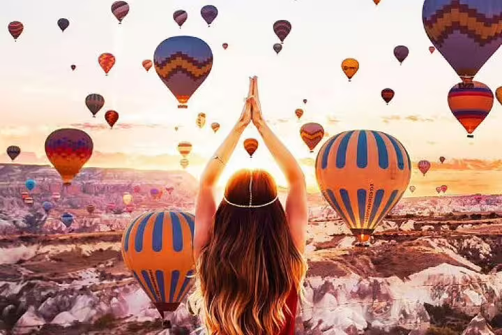 A woman practices yoga amidst a breathtaking view of hot air balloons filling the sky over Cappadocia at sunrise.