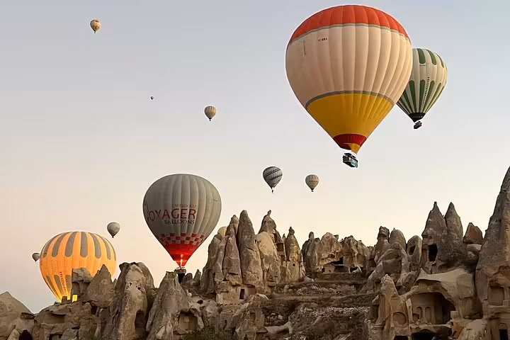 Hot air balloons flying over Cappadocia fairy chimneys at sunrise, highlight of a private day tour with guide and car