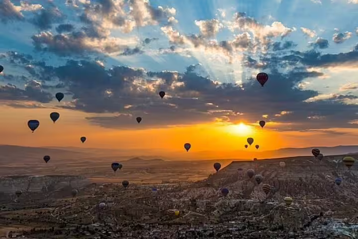 Dozens of colorful hot air balloons soar against a breathtaking Cappadocia sunrise, offering a magical aerial view.