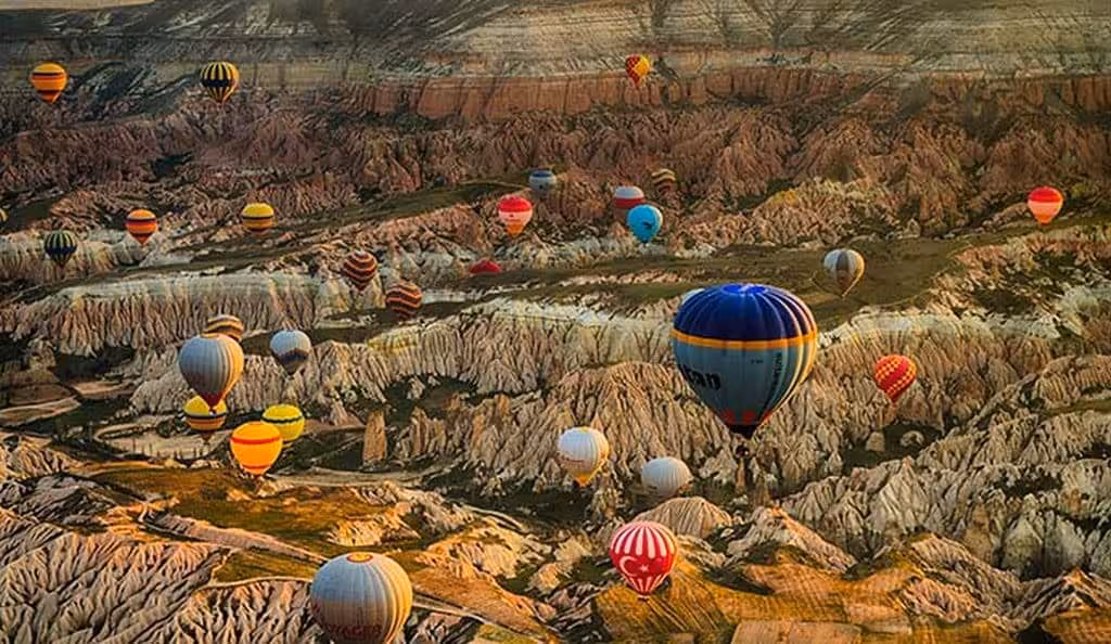 Colorful hot air balloons floating above Cappadocia valleys and rolling landscape