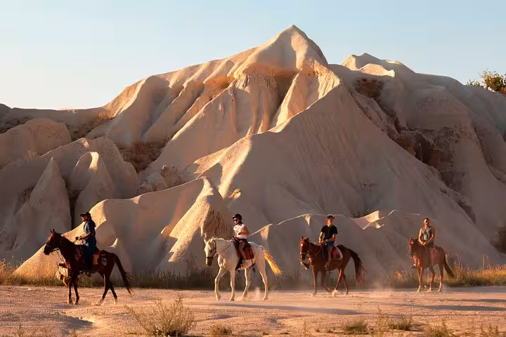 Group horseback riding past Cappadocia fairy chimneys at sunset, scenic 2-hour guided trail experience