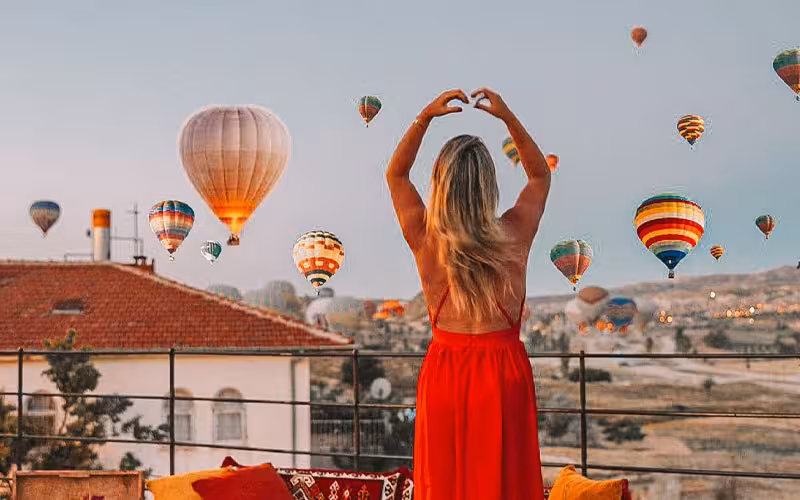 Traveler in a red dress watching hot air balloons from a Cappadocia viewpoint