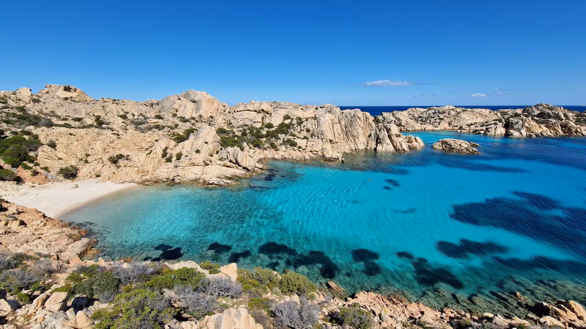 Aerial view of Cala Coticcio's pristine turquoise waters and rugged cliffs on Caprera Island hiking adventure.