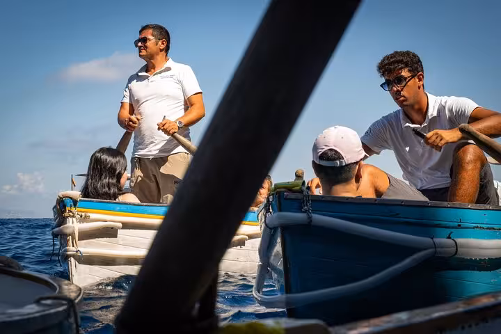 Tourists enjoy a sunny boat ride near Capri's stunning coastline, guided by local boatmen during the Blue Grotto tour.