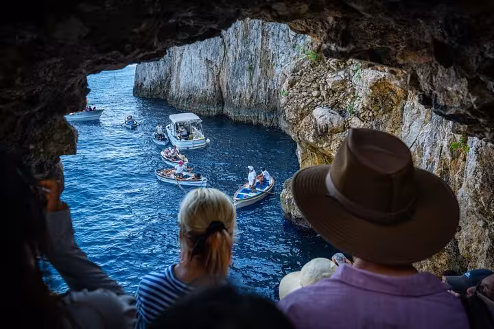 Visitors observing boats entering the Blue Grotto through a rocky archway on the Capri and Anacapri excursion.