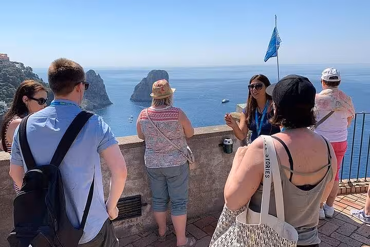 Tourists enjoy a guided tour of Capri overlooking the stunning Faraglioni rock formations under a clear blue sky.