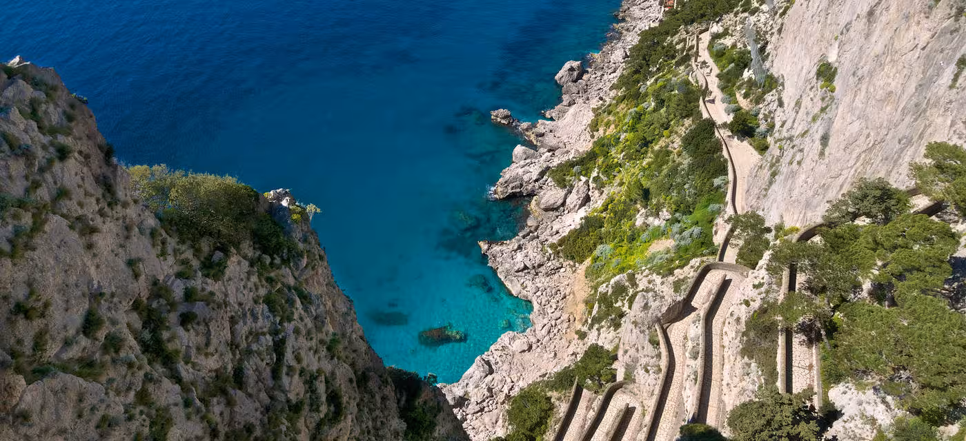 Aerial view of the winding Via Krupp path leading down to the crystal-clear waters of Capri's coastline.