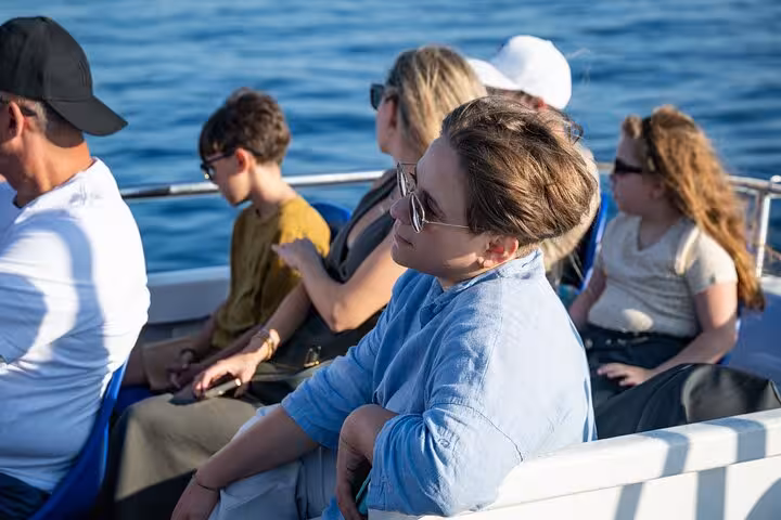 Tourists enjoying a scenic boat ride on a Capri and Blue Grotto full-day tour under the bright blue sky.