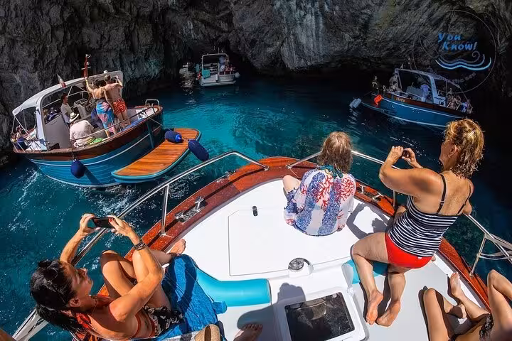Visitors capture stunning views of Capri's grottoes from a boat, experiencing an exclusive Sorrento tour.
