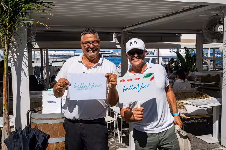 Two smiling tour guides holding signs, welcoming visitors to the Capri and Blue Grotto full-day excursion.