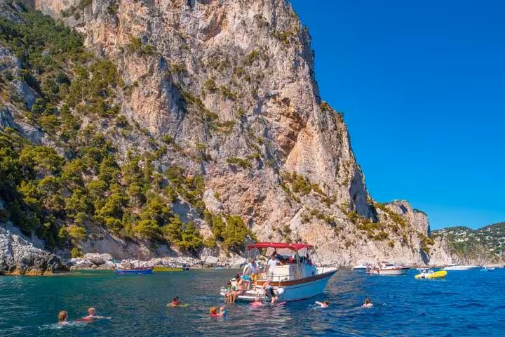 Tourists enjoy swimming near a boat with stunning cliffs on the Capri boat tour with Blue Grotto experience.