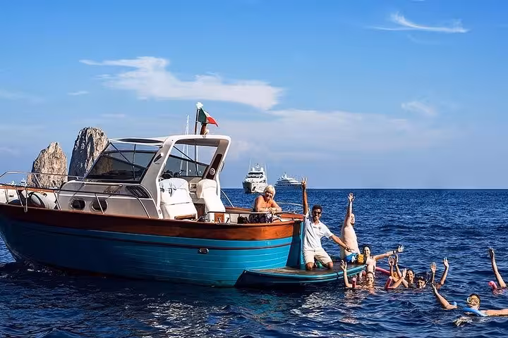 Happy group swimming and relaxing by a boat under clear skies on the Capri boat tour with Blue Grotto adventure.