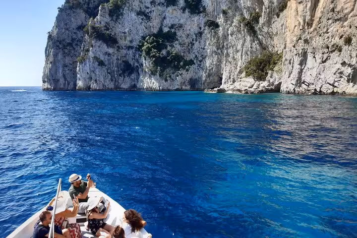 Tourists enjoying a boat ride near Capri's stunning cliffs and clear blue sea, exploring the famous grottoes.