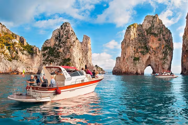 Luxurious boat cruising through the iconic Faraglioni cliffs on a small group excursion from Positano to Capri.