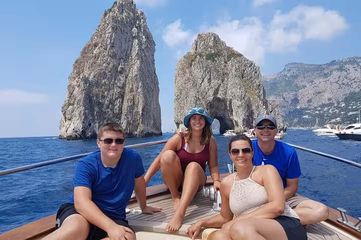 A small group enjoys a Capri boat excursion with scenic views of the Faraglioni rocks near Positano.