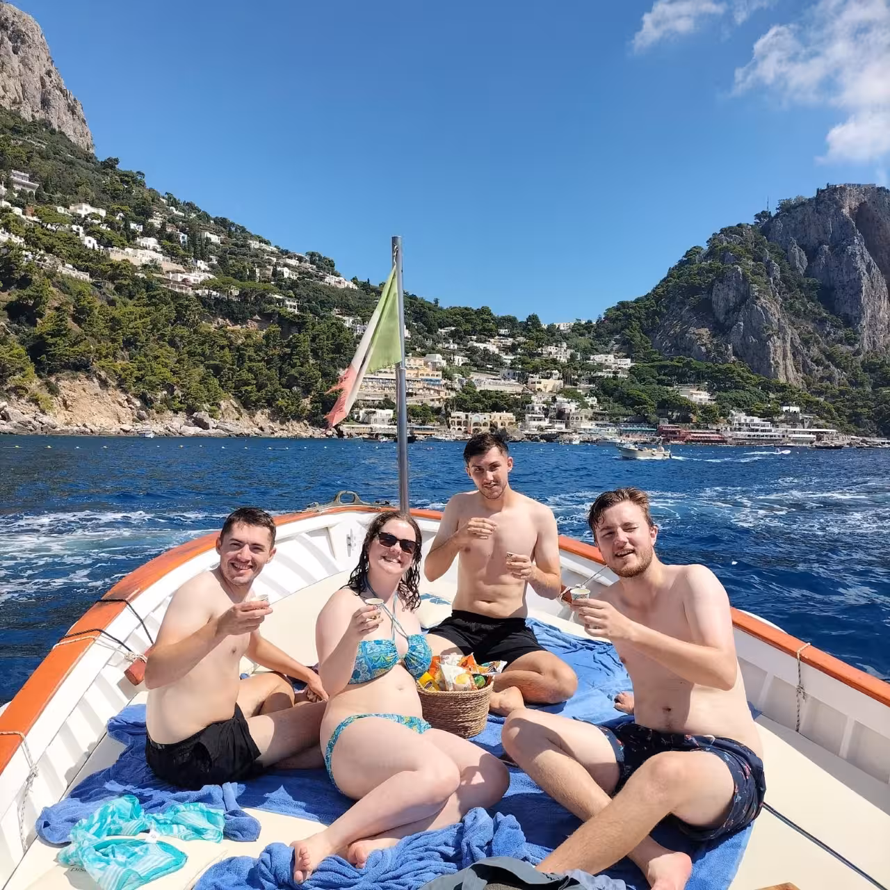 Group enjoying drinks on boat with Capri coastline views, part of Best of One Day boat tour and minibus experience