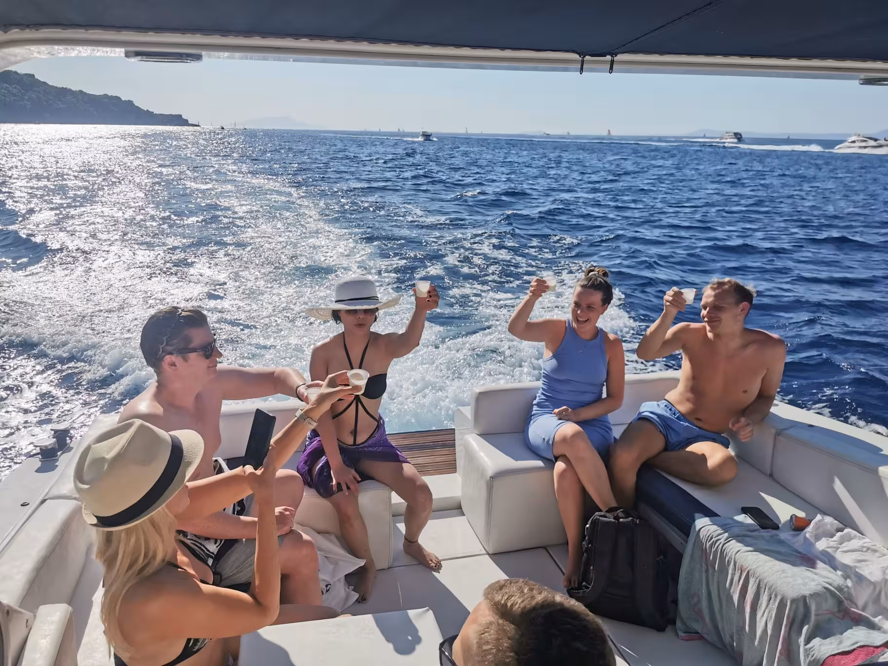 Group of friends enjoying limoncello on a scenic Capri boat tour from Sorrento, under a sunny sky.