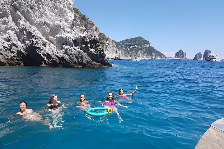Guests swimming in crystal-clear sea by dramatic cliffs on a private full-day boat tour, sea day freedom