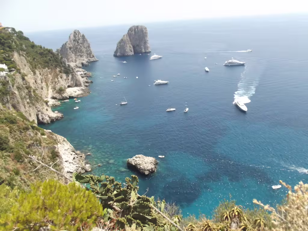 Panoramic view of Capri’s Faraglioni cliffs and yachts on turquoise Tyrrhenian Sea during a full-day boat tour