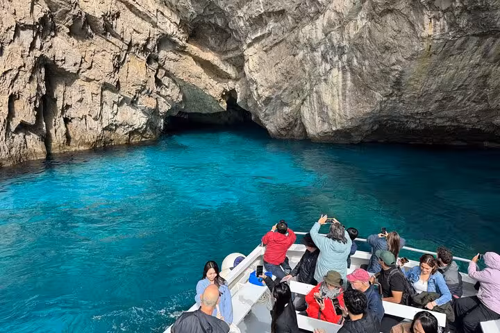 Tourists on a boat entering a stunning sea cave with turquoise water during a Capri and Anacapri Faraglioni cruise.