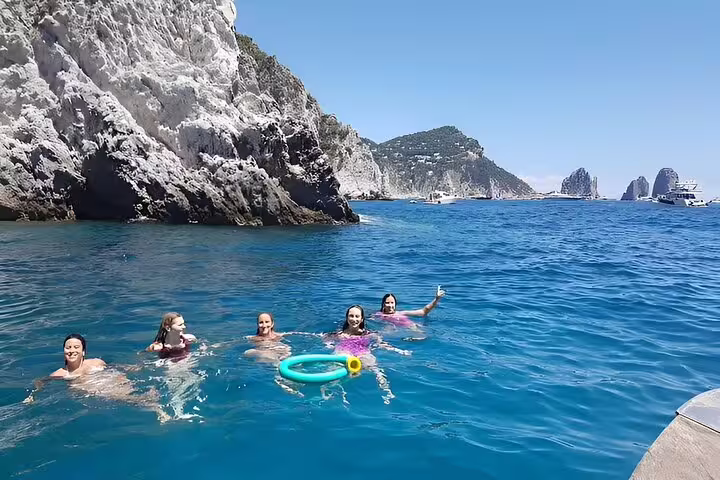 Guests swimming in blue sea near Faraglioni rocks on Capri Essence private classic boat tour, 4h