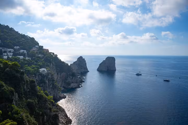 Stunning view of Capri's iconic Faraglioni rock formations with turquoise sea and lush cliffs under a bright sky.