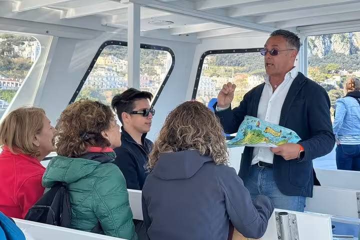 Tour guide explaining Capri attractions to visitors aboard a boat, highlighting Faraglioni and grottoes.