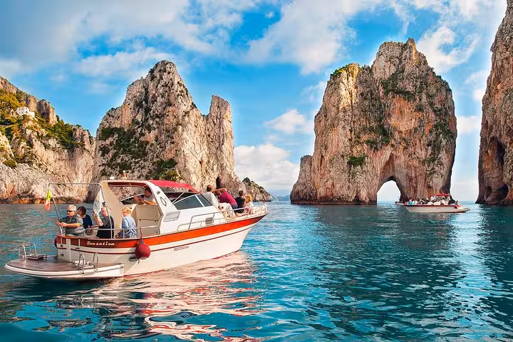 Tourists enjoy a scenic boat ride near the iconic Faraglioni rocks on a Capri Island day excursion from Sorrento.