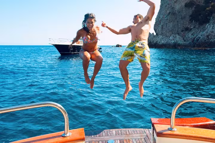 Two people joyfully jumping off a boat into the clear blue waters during Capri Island boat excursion from Amalfi.