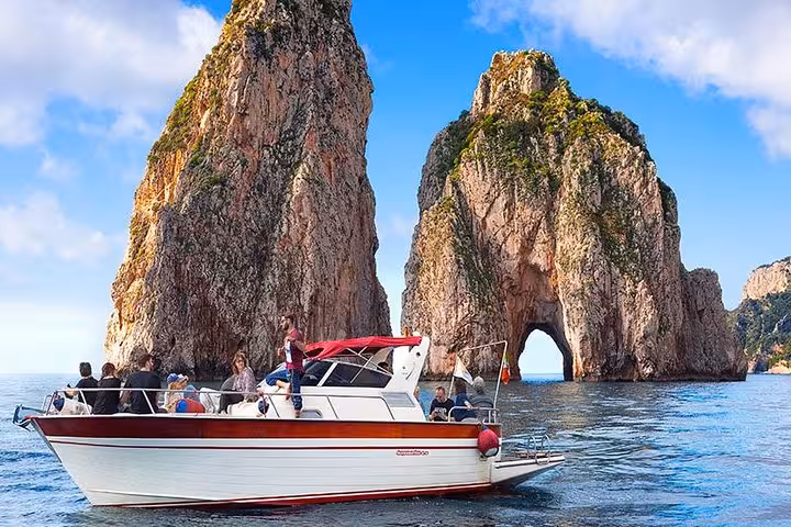Boat touring near the iconic Faraglioni rocks during a Capri Island excursion from Sorrento.