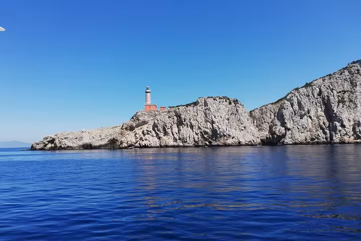 Picturesque lighthouse perched on rocky cliffs overlooking the serene blue waters near Capri during a guided tour.