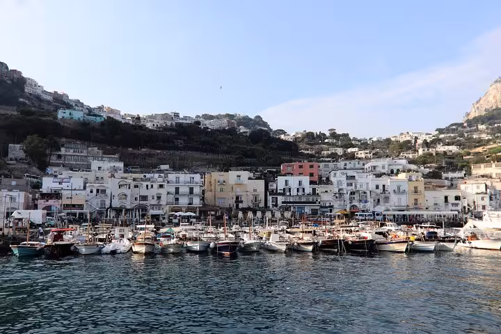 Scenic view of Capri's Marina Grande harbor with vibrant boats and hillside buildings, perfect for a Faraglioni cruise tour.