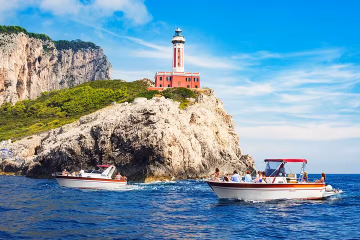 Tourists on classic Gozzo boats enjoy views of Capri's iconic lighthouse and rugged coastline.