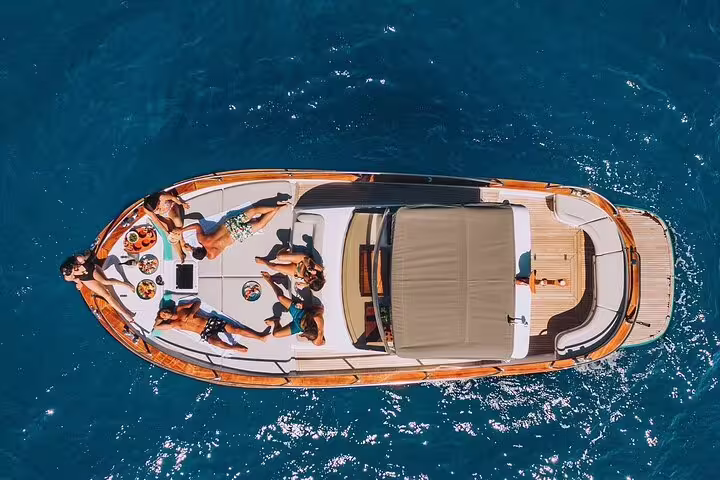 Aerial view of a wooden luxury boat with sunbathing guests on turquoise waters near Capri