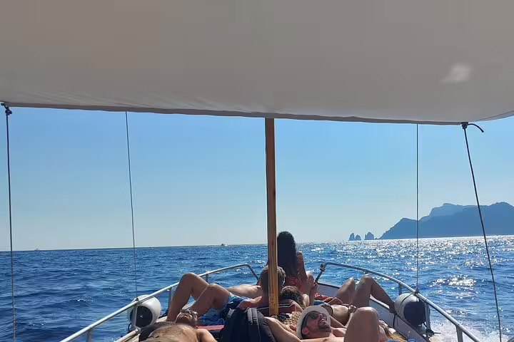 Guests relaxing on a private boat tour full day cruise, sparkling sea views and Capri coastline ahead