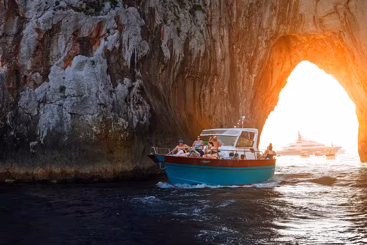 Group enjoying a scenic boat ride through the glowing arch of Faraglioni at sunset on a Capri evening tour from Sorrento.