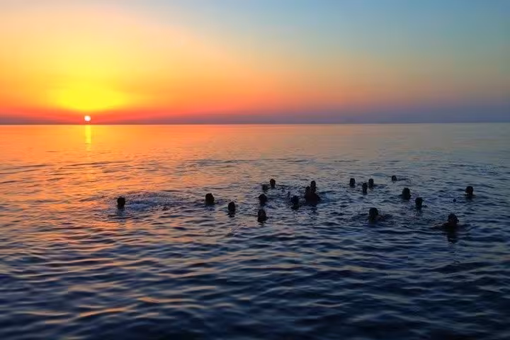 Silhouettes of swimmers enjoying a vibrant sunset swim in the Mediterranean during a Capri boat tour.