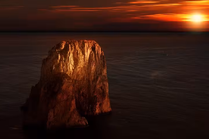 Dramatic sunset over Faraglioni rock formations during Capri boat tour from Sorrento, highlighting golden hues.
