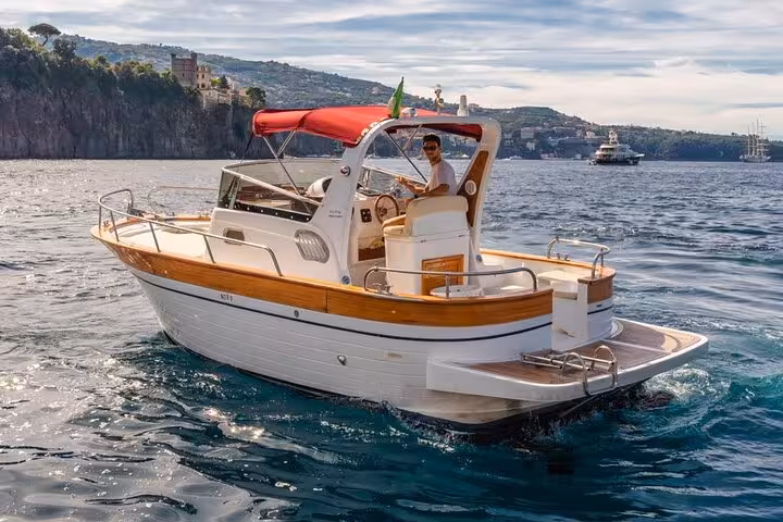 Captain steering a typical Gozzo 750 boat on a private tour from Sorrento to Positano across the sparkling sea.