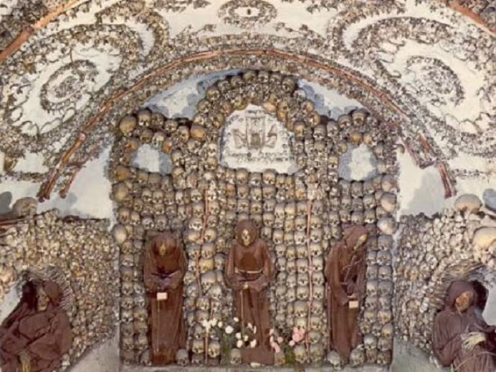 Macabre Capuchin Crypt in Rome decorated with skulls and bones, featuring robed monks in an underground chapel