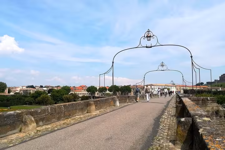 Tourists walk along the historic bridge in Carcassonne on a sunny day, ideal for exploring with a local guide.