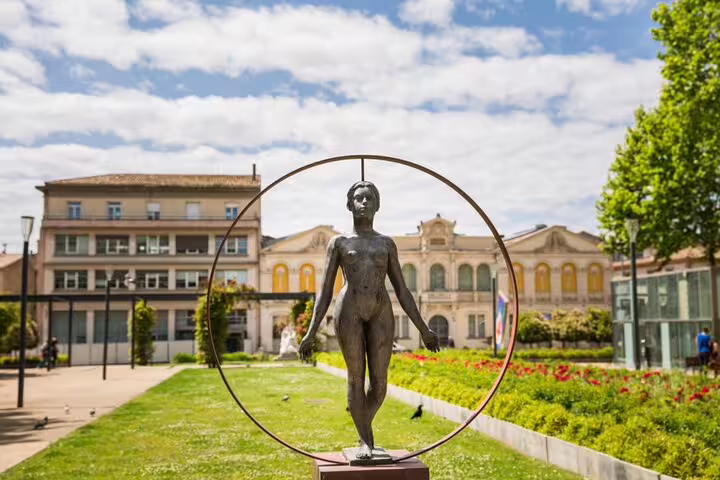 Bronze female sculpture inside a large circular ring in a sunny public garden in Carcassonne