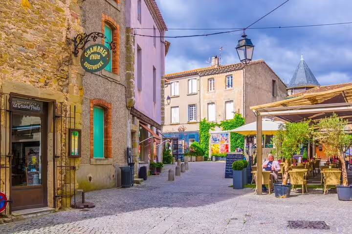Cobblestone street in Carcassonne medieval city with stone buildings, outdoor café, and guesthouse sign