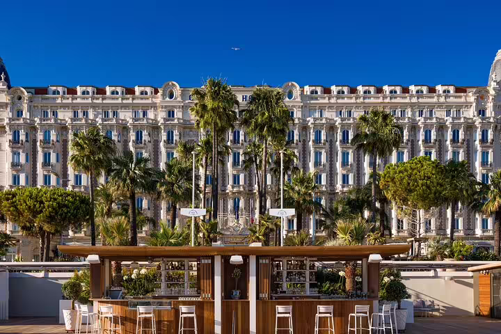Carlton Hotel façade with palm trees and outdoor beach bar in Cannes, French Riviera