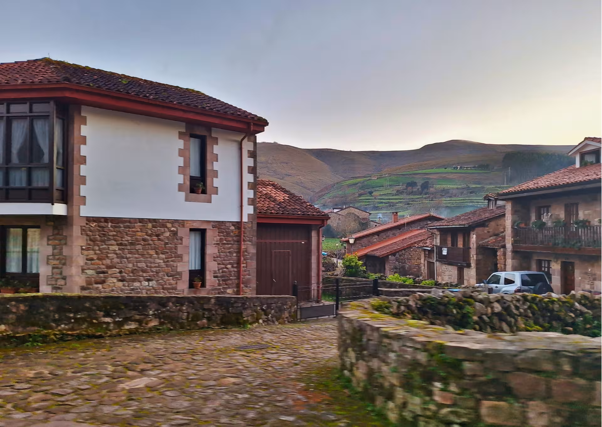 Cobblestone street lined with traditional stone houses and green hills in Carmona Cantabria village tour