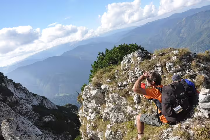 Hiker with backpack resting on rocky Carpathian mountain ridge overlooking vast green valley below
