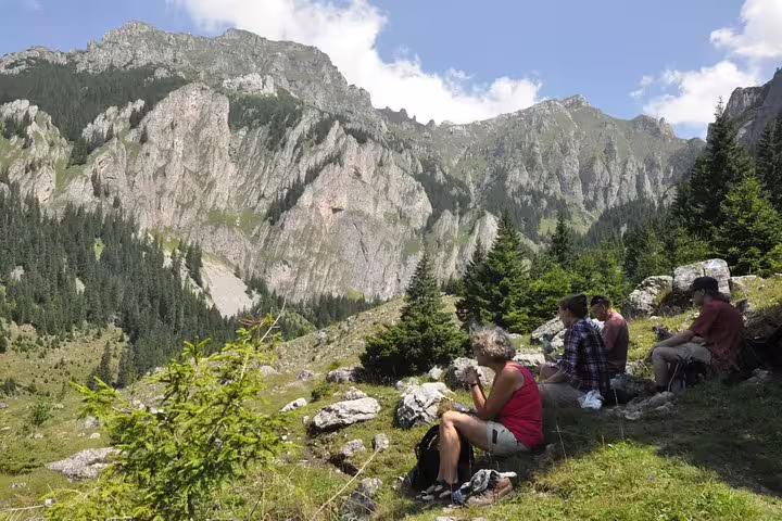 Hikers resting on rocky alpine meadow with dramatic Carpathian Mountain cliffs and forest in background