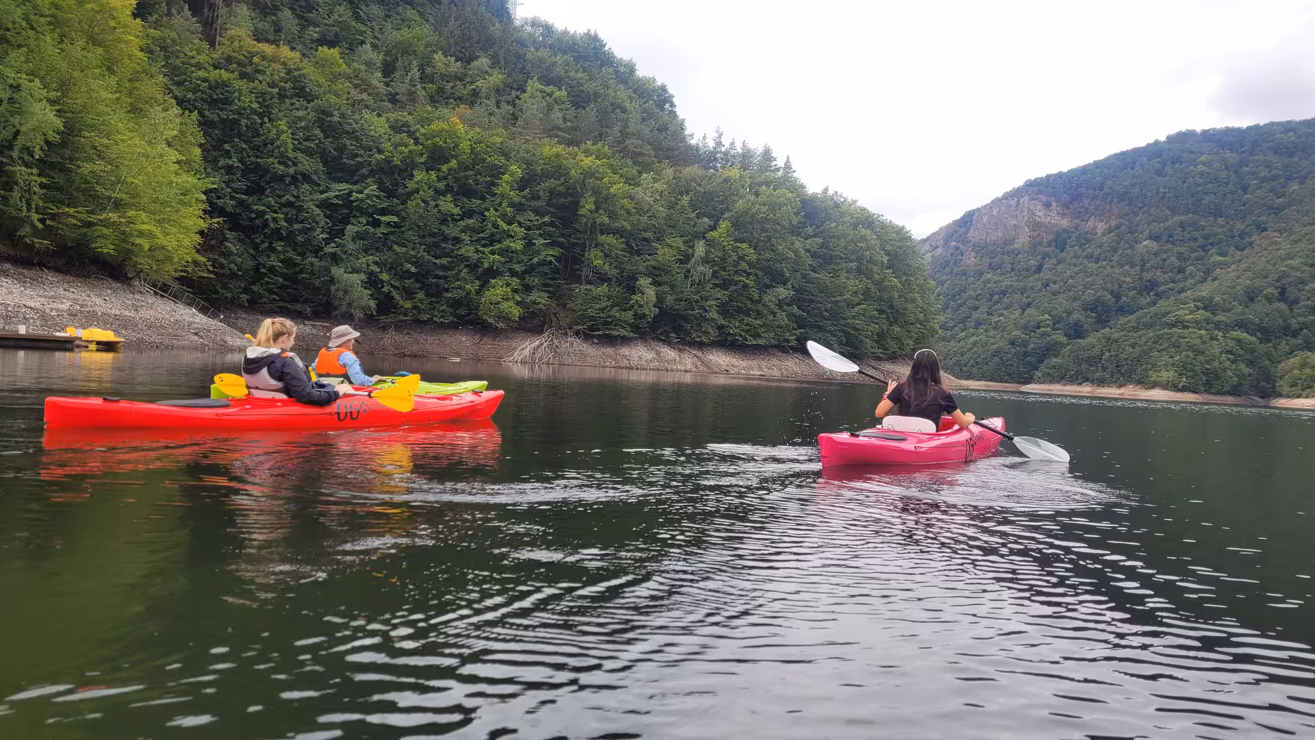 Three kayakers paddling colorful kayaks on a calm mountain lake surrounded by lush Carpathian forest