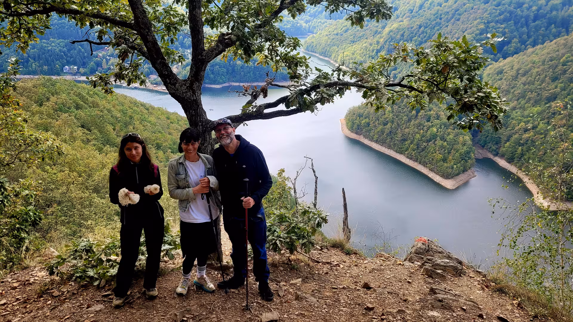 Three hikers posing on a rocky overlook above a winding lake surrounded by forested Carpathian hills