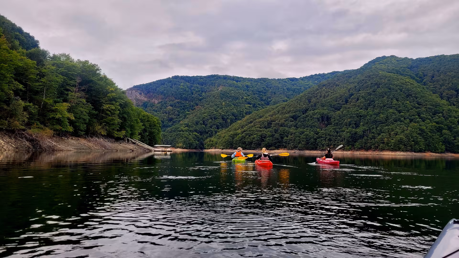 Three kayakers paddling colorful kayaks on a calm mountain lake surrounded by lush Carpathian forest